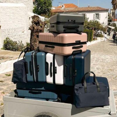 A cart stacked with multiple suitcases and duffle bags on a street.